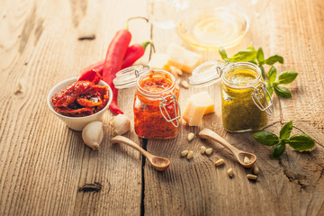 Red pesto and ingredients on a rustic wooden table This particular pesto is prepared by an Italian traditional recipe with dried tomatoes in olive oil, parmesan cheese, olive oil, pine nuts