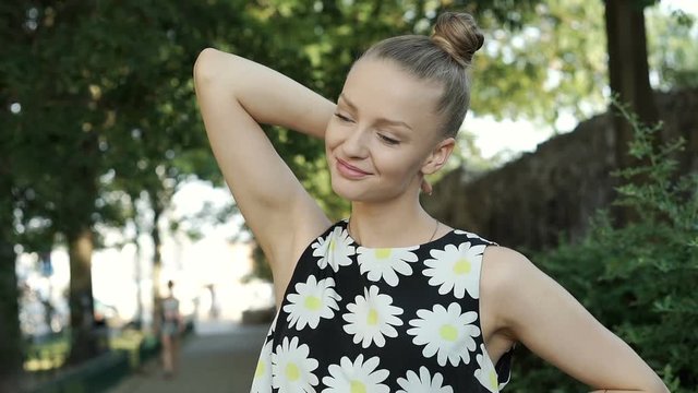 Pretty, blonde girl in floral shirt standing in the park and relaxing, steadycam shot
