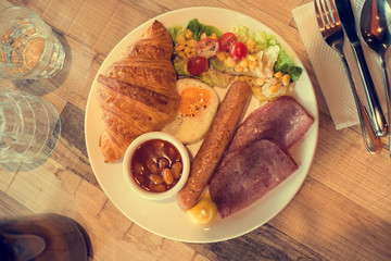 English breakfast with fried eggs, bacon, sausages, beans, toasts and fresh salad