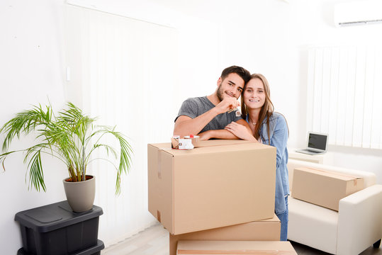 cheerful and happy young couple holding the keys of their new home with moving cardbox during move into new apartment