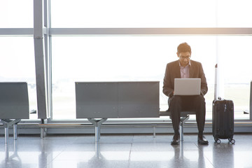 Asian Indian business man sitting on chair and using laptop while waiting his flight at airport.