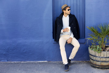 Guy in hat and sunglasses sitting against blue wall