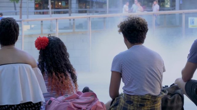 People with their backs looking at the jets of water in the square