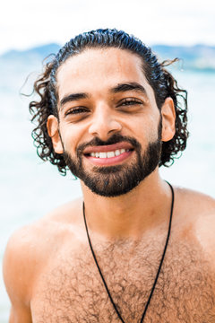 Close-up portrait of a sweet smiling Arab male. Tanned, a guy with curly wet hair on the beach, white teeth, positive, having fun relaxing on a tropical island, sports body, summer, round neck pendant