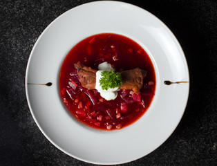A real Russian borsch on a white plate and black marble with a rib