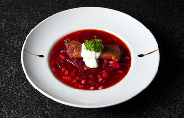A real Russian borsch on a white plate and black marble with a rib