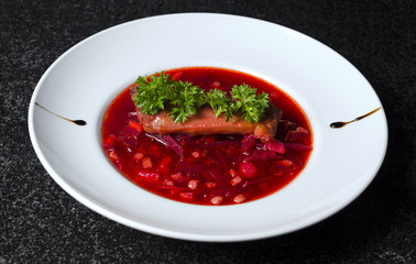 A real Russian borsch on a white plate and black marble with a rib