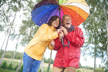 Wet couple hiding under colorful umbrella