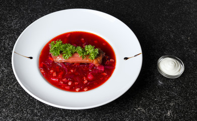 A real Russian borsch on a white plate and black marble with a rib