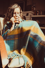 Winter cold sickness concept. Young freezing woman sitting in comfortable modern chair with mug of...