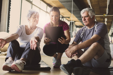 Senior couple in rehabilitation center. Personal trainer writing records exercises