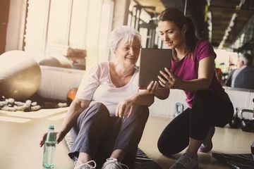 Foto op Plexiglas Senior woman workout in rehabilitation center. Personal trainer showing something  on digital tablet. © liderina