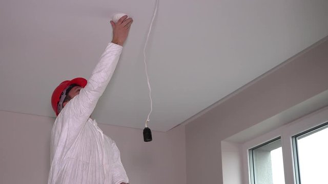 Skilled electrician man mount fire smoke alarm system on ceiling