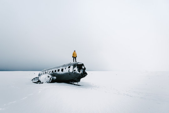 Person In Yellow Jacket Standing On Top Of A Plane Wreck In Iceland During Winter