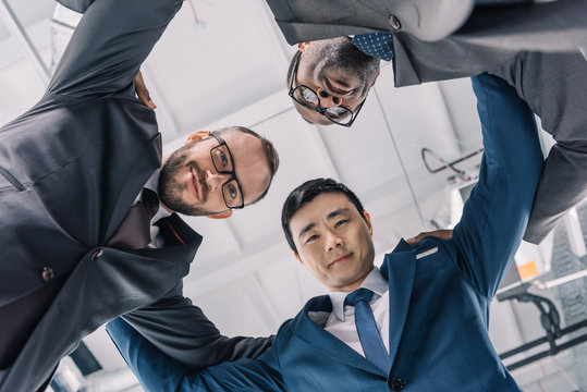 Group Of Multiethic Businessmen Holding Each Other And Looking Down At Camera