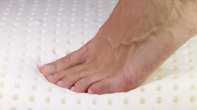 Piede sta premendo su un materasso in memory foam. Schiuma di memoria.