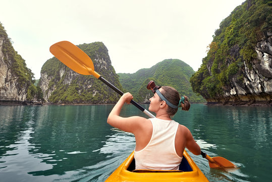 Woman paddling kayak in calm bay among picturesque karst mountains