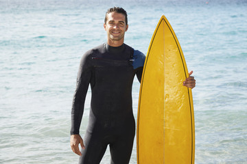 Happy surfer in wetsuit holding surfboard, portrait