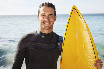 Smiling surfer dude in wetsuit holding surfboard