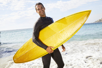 Happy surfer with board on beach, wearing wetsuit