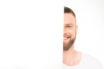 'Happy man standing behind and looking out of large blank white banner with copy space, isolated on white