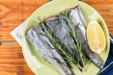 Hake fish with rosemary and lemon on the green plate above wooden board