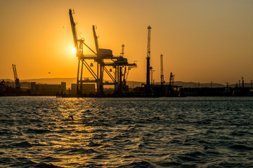 Obraz premium The silhouette of the port of Novorossiysk at sunset and the reflection of sunset in the waves of the uneasy Black sea