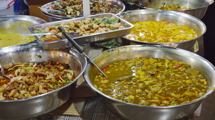 variety Thai curry and food displays in stainless basin for take home on market