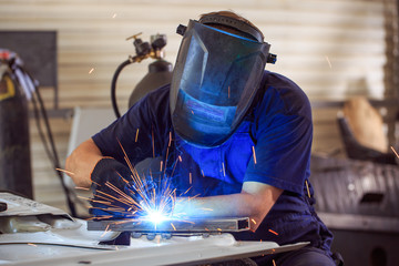 Male in face mask welds with argon-arc welding
