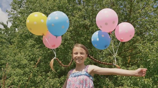 Cheerful and pretty girl smiling with colorful balls attached to her hair and braids on her head. Funny idea with balloons.