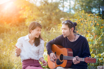 Fototapeta premium younger asian man and woman relaxing playing guitar in park
