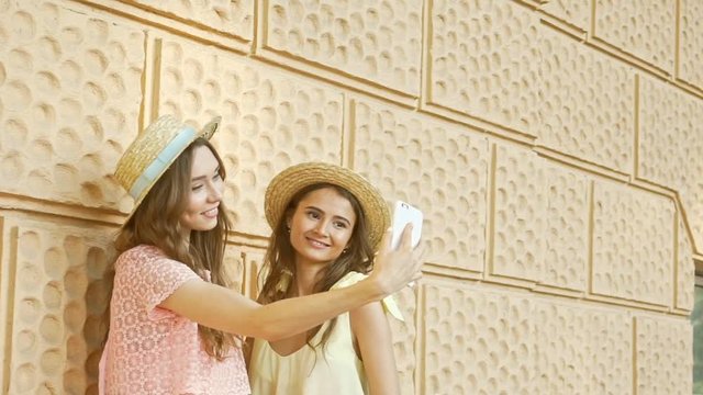 Young happy friends in hats and dresses making selfie on smartphone near bicycle in the street