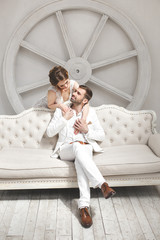Obraz premium Chic wedding couple groom and bride posing in a white Studio. Happy couple laughing. White dress. White suit. Youth. Wedding. Chandelier. Sofa. The door.