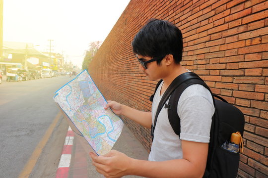 Rear view of handsome young Asian backpacker exploring the map for right direction at Chiang Mai , Thailand. Travel and tourism asia concept.