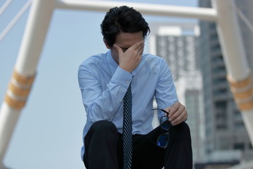 Front view of frustrated young Asian business man takes off glasses and close his eyes. he is...