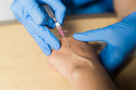 Nurse Starting IV On Patient's Hand In Hospital