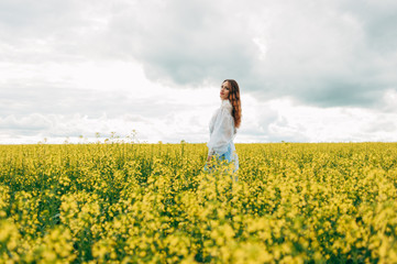 Fototapeta premium Beautiful girl in a dress among yellow flowers in a field