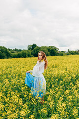 Fototapeta premium Beautiful girl in a dress among yellow flowers in a field