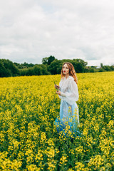 Fototapeta premium Beautiful girl in a dress among yellow flowers in a field