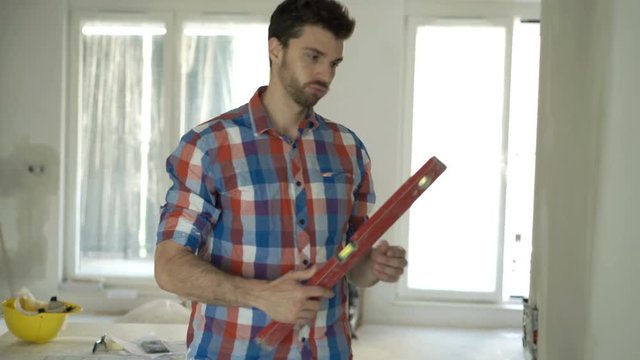 Young man with blueprints checking wall with level at new home 

