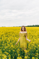 Fototapeta premium Beautiful girl in a dress among yellow flowers in a field