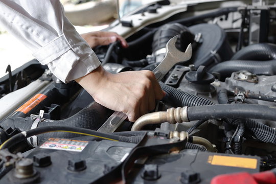 Hands of mechanic with wrench repairing engine of motor car under car hood.