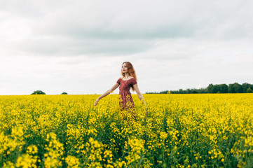 Fototapeta premium Beautiful girl in a dress among yellow flowers in a field