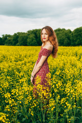 Obraz na płótnie Canvas Beautiful girl in a dress among yellow flowers in a field