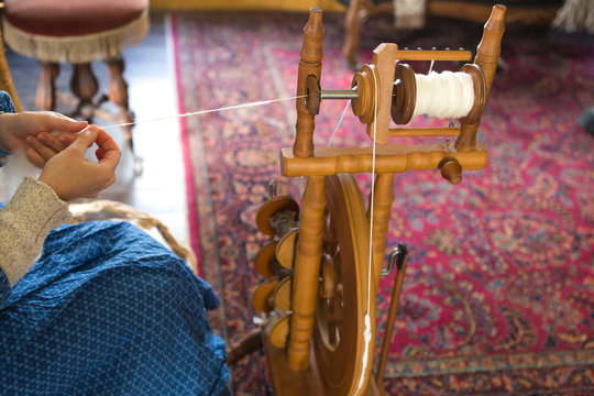 Woman sitting using vintage loom and spinning wheel