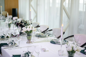 covered festive table for a wedding dinner in a white summer style with bouquets of tulips.