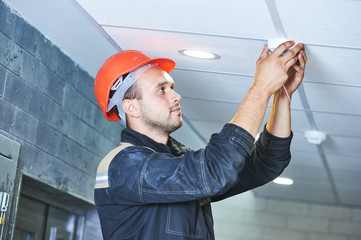 worker installing smoke detector on the ceiling