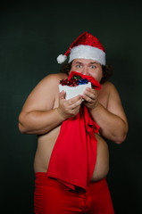 Funny guy without a shirt in a Santa suit. Cheerful fat Santa Claus. 