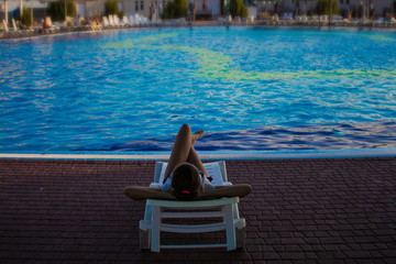 Fototapeta premium Young girl is resting on a sun lounger near a swimming pool. Vacation concept