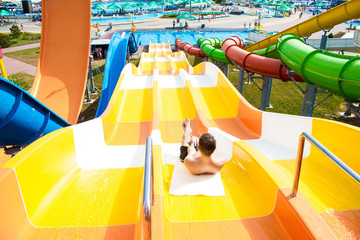 Young cheerful man has fun on vacation on a slide in the water park. Hot summer day